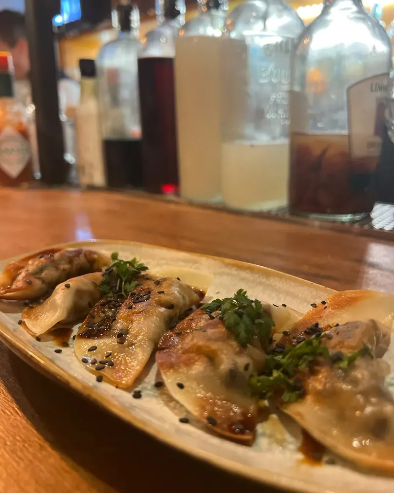 Gyozas shiitaké et ricotta poêlés, sésame noir et cerfeuil, devant les bouteilles du bar