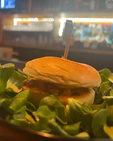 Mini burger bœuf, chorizo et cheddar sur lit de mâche, le bar éclairé en arrière-plan