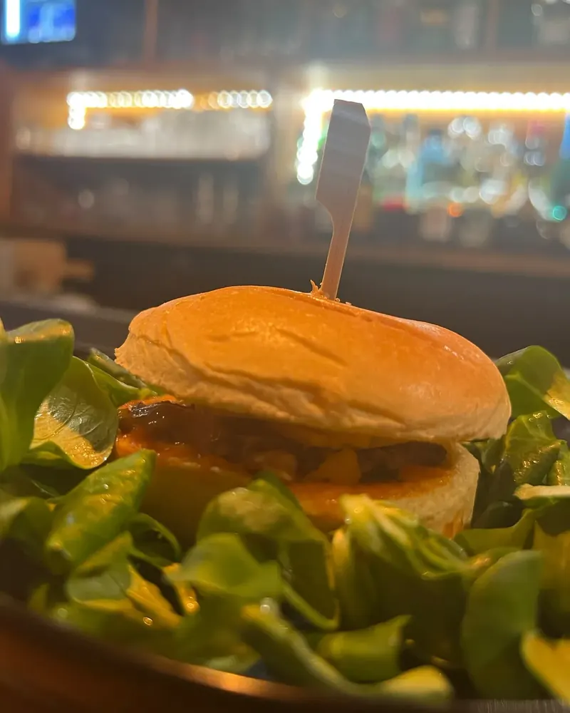 Mini burger bœuf, chorizo et cheddar sur lit de mâche, le bar éclairé en arrière-plan