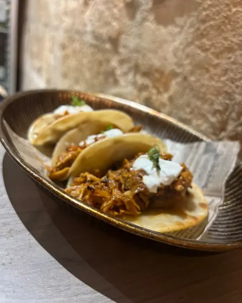 Trois tacos de porc effiloché à la sauce rouge et crème, devant le mur en pierre du Phantom